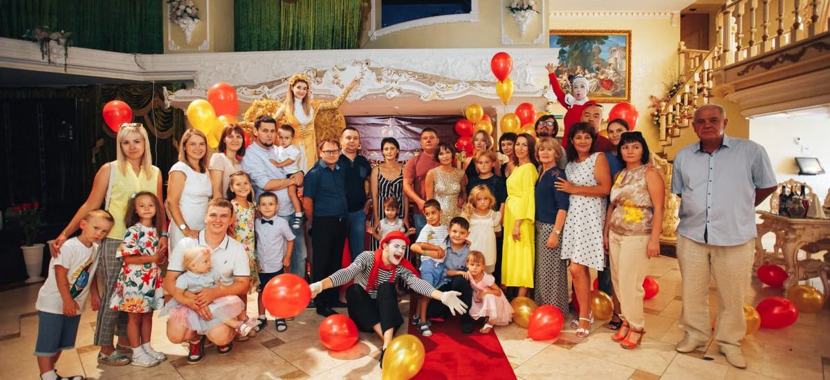 Group of people enjoying a festive indoor party with clowns and colorful balloons.