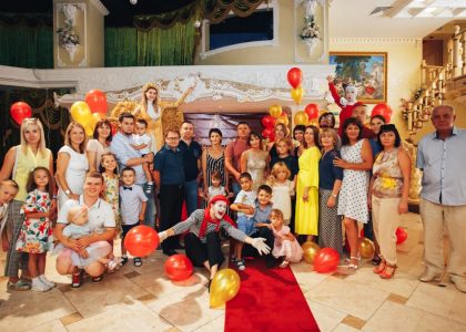 Group of people enjoying a festive indoor party with clowns and colorful balloons.